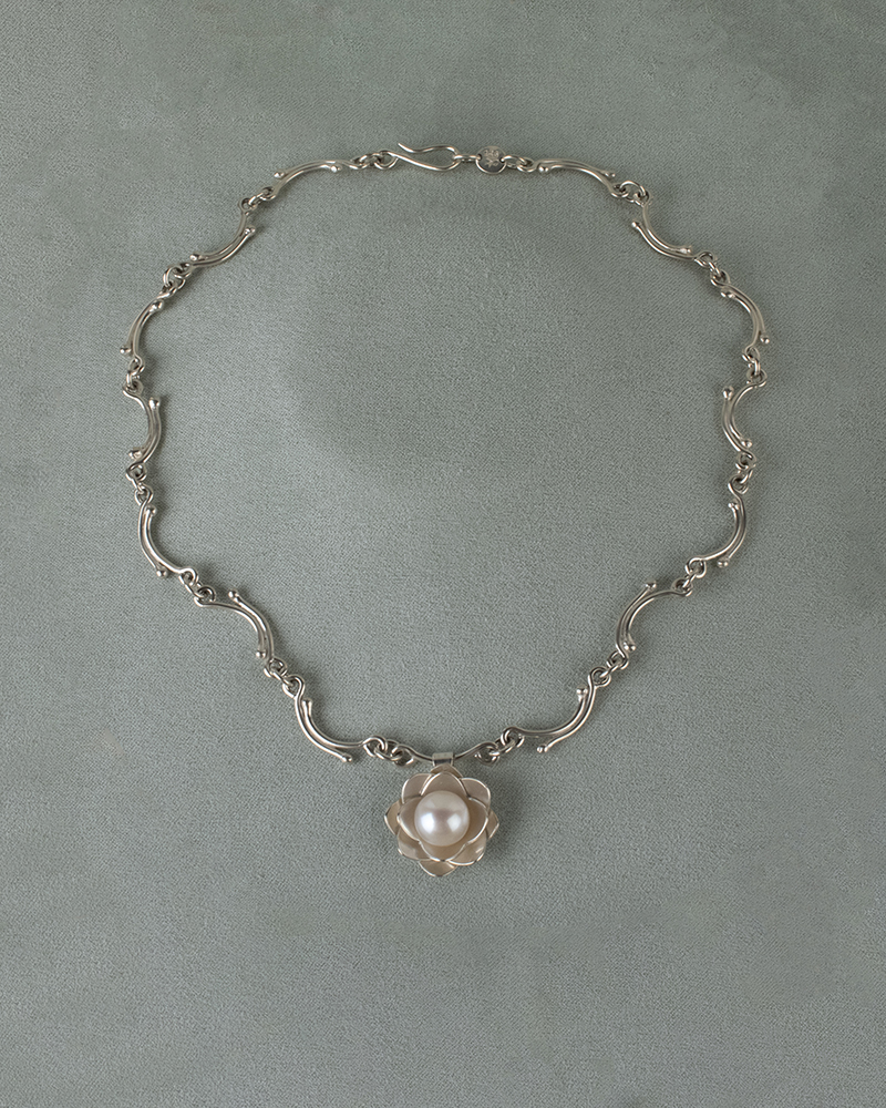A closeup of a silver necklace with a pearl pendant